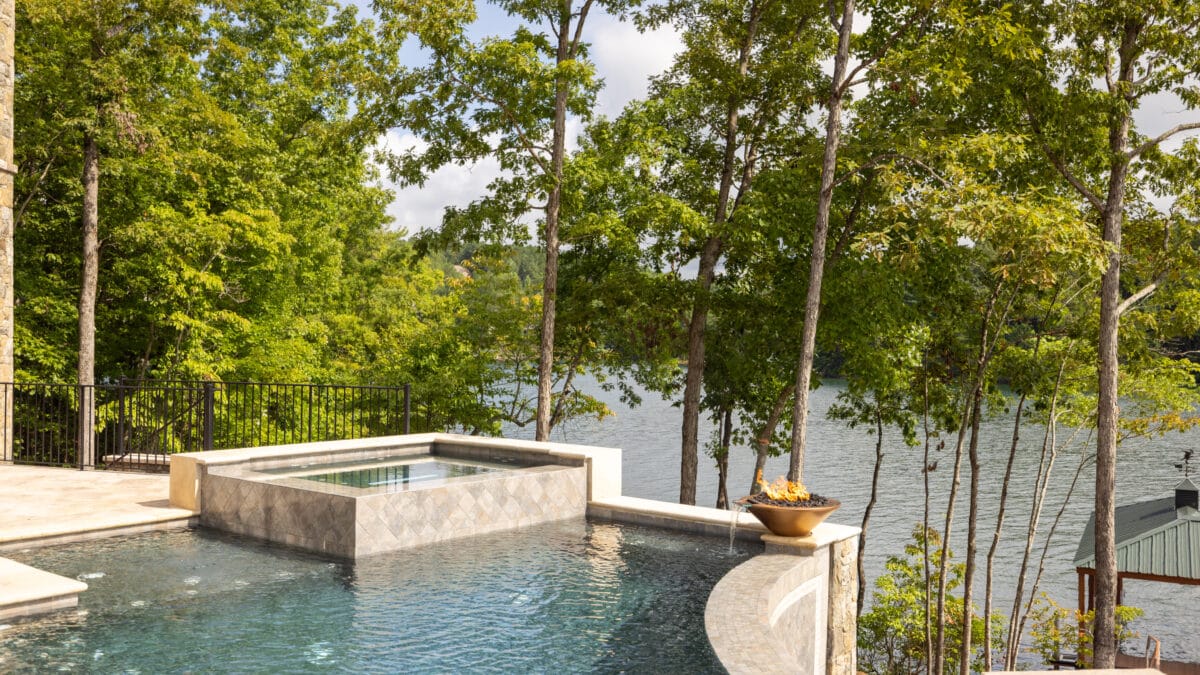 Infinity pool with a stone edge and a view of a lake surrounded by trees.