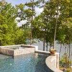 Infinity pool with a stone edge and a view of a lake surrounded by trees.