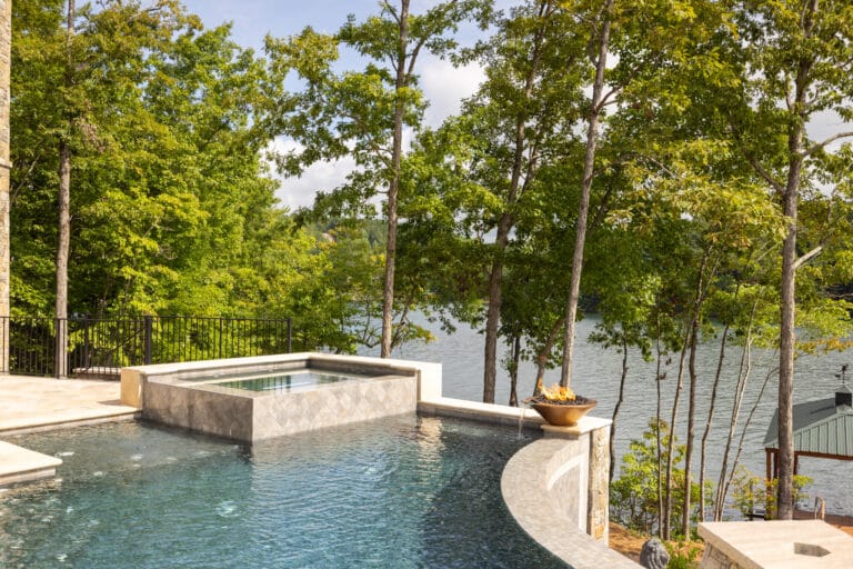 Infinity pool with a stone edge and a view of a lake surrounded by trees.