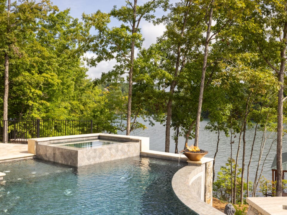 Infinity pool with a stone edge and a view of a lake surrounded by trees.