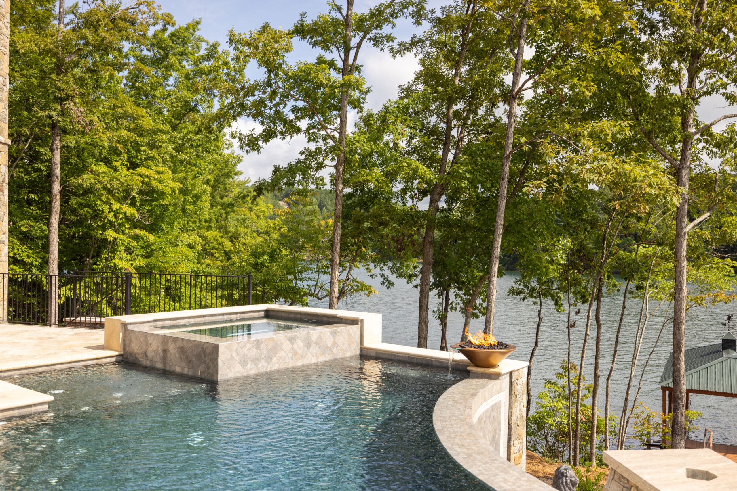 Infinity pool with a stone edge and a view of a lake surrounded by trees.